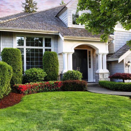 Beautiful home exterior in evening with manicured green lawn and blooming red flowers in bushes