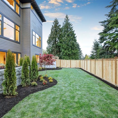 Luxurious contemporary three-story wood siding home exterior in Bellevue. Nice backyard landscape with well kept lawn flower beds and wooden fence. Northwest USA